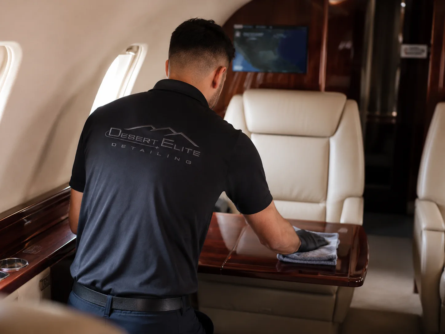 Professional detailer wiping a polished wood table inside a private jet cabin