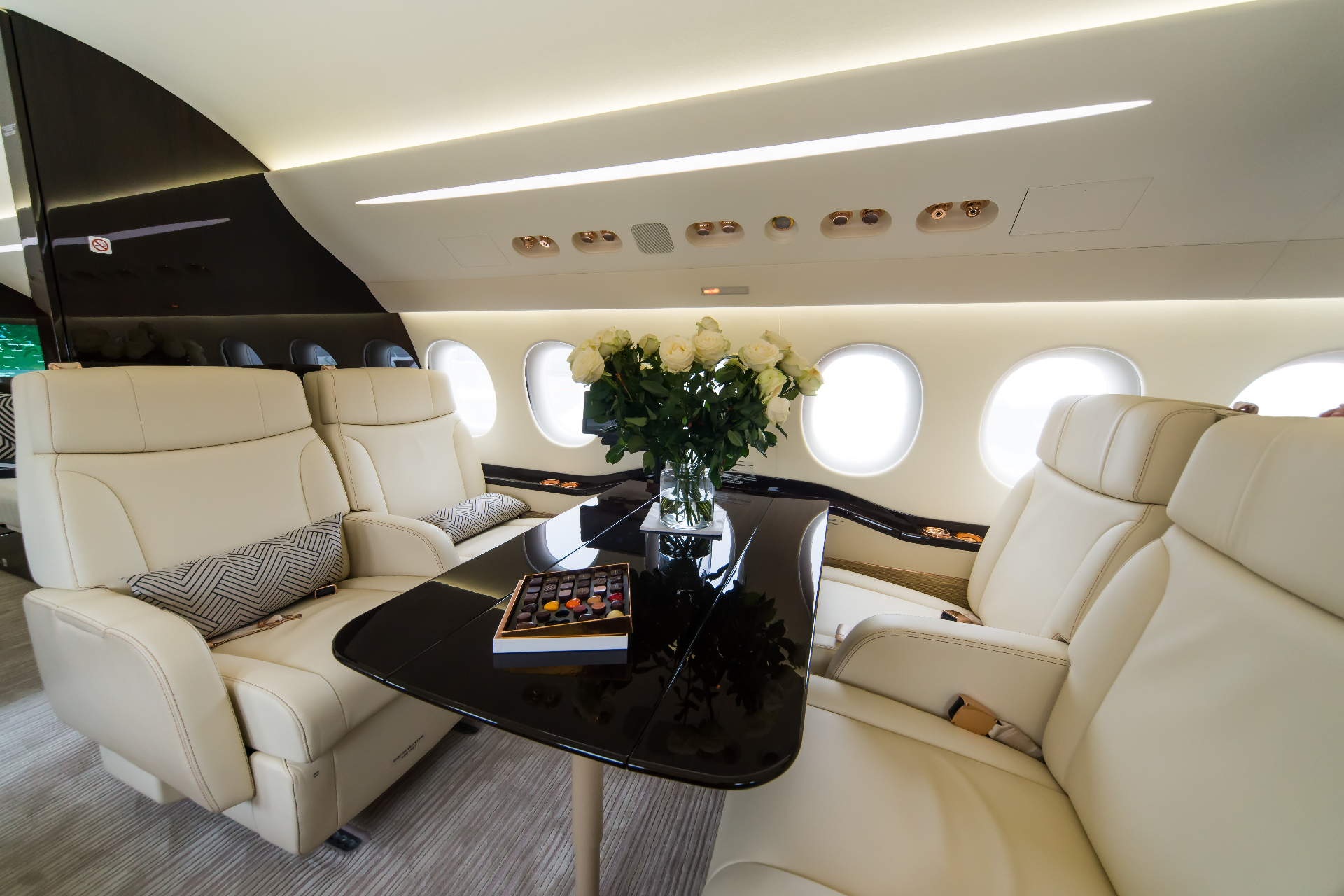Pristine private jet cabin with cream leather seating, fresh roses, and chocolates on a polished table