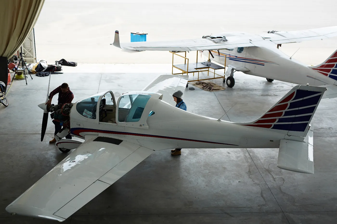 Two technicians servicing a white prop plane inside an open hangar